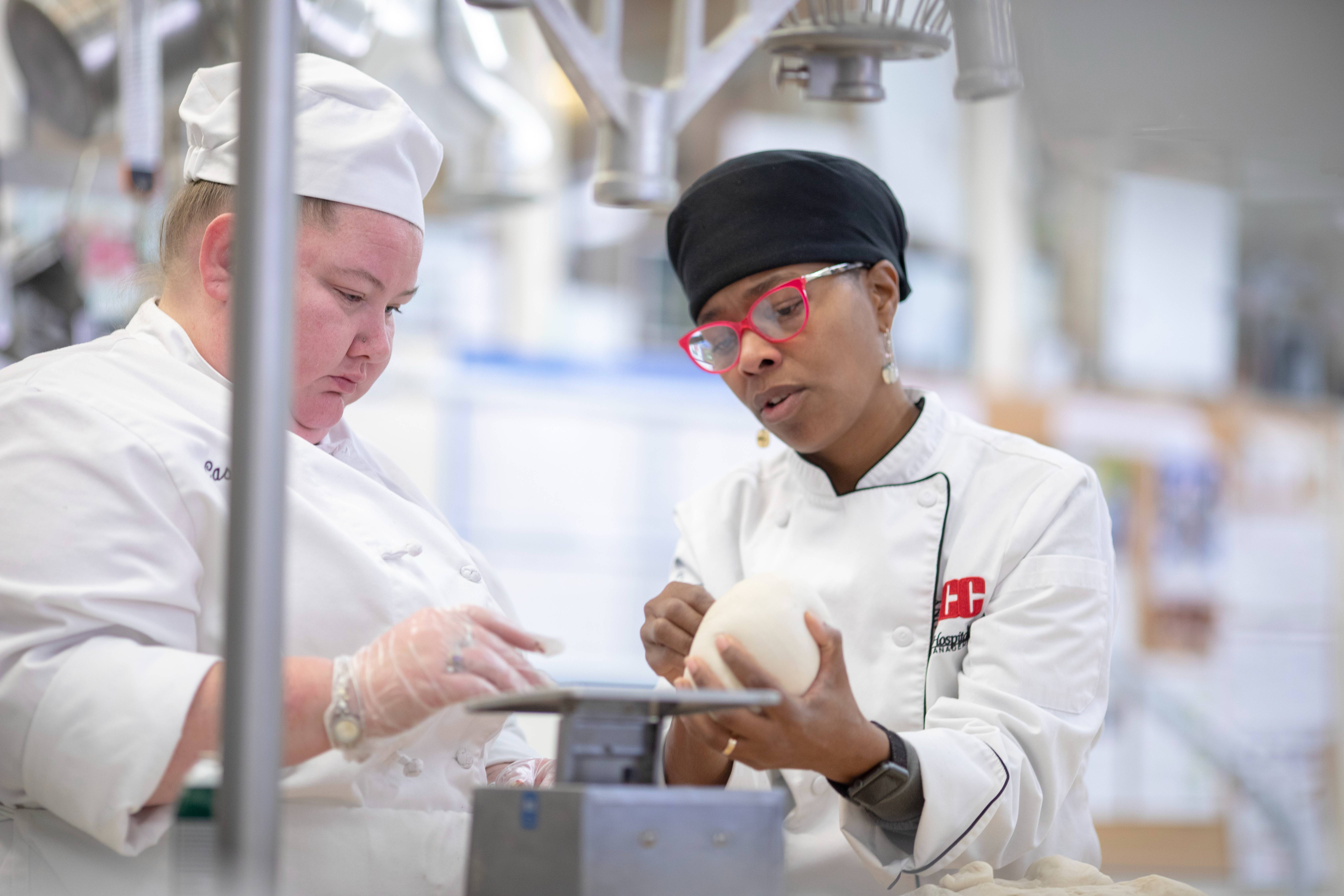 Two students weighing dough in an industrial kitchen