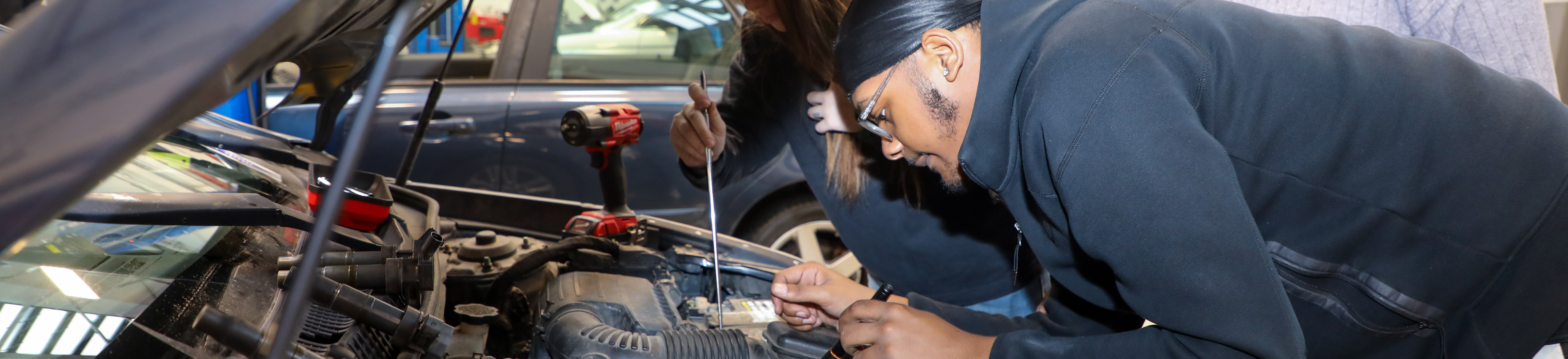 Two mechanics working under the hood of a car.